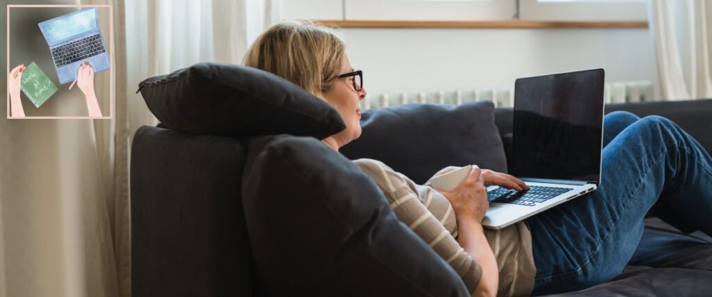 Woman using a laptop while reclining on a sofa with a cup, illustrating creative work from home.