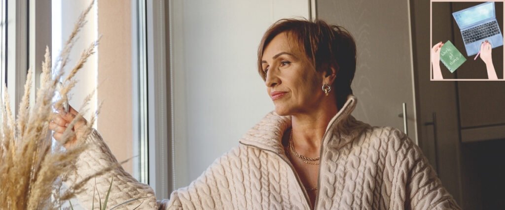 Woman in a knitted sweater looking out of a window at home.